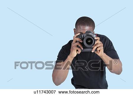 Stock Photo - African American young man taking photo through digital camera over blue background. Fotosearch