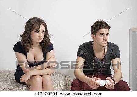 Stock Image - Angry young woman looking at man holding video game controller. Fotosearch