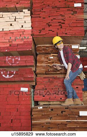 Asian female industrial worker standing on stacked wooden planks holding tablet PC View Large Photo Image Stock Photo - Asian female industrial worker standing on stacked wooden planks holding tablet PC. Fotosearch