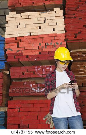 Asian female industrial worker using cell phone with stacked wooden planks in background View Large Photo Image Stock Photography - Asian female industrial worker using cell phone with stacked wooden planks in background. Fotosearch
