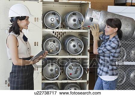 Asian woman looking at female industrial worker carrying propane cylinder View Large Photo Image Stock Photo - Asian woman looking at female industrial worker carrying propane cylinder. Fotosearch
