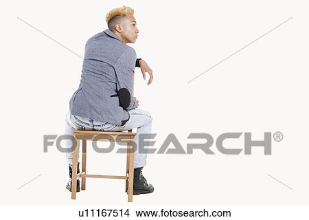 Back view of teenage boy sitting on chair as he looks away over gray background View Large Photo Image Picture - Back view of teenage boy sitting on chair as he looks away over gray background. Fotosearch