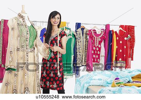 Stock Photo - Beautiful Indian female dressmaker looking away while working on traditional outfit. Fotosearch