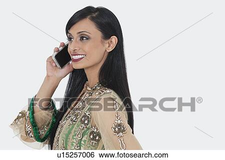 Beautiful young Indian woman in traditional wear attending phone call over gray background View Large Photo Image Stock Photograph - Beautiful young Indian woman in traditional wear attending phone call over gray background. Fotosearch