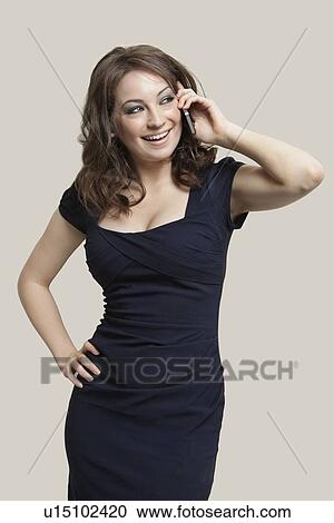 Beautiful young woman communicating on cell phone while looking away over gray background View Large Photo Image Stock Image - Beautiful young woman communicating on cell phone while looking away over gray background. Fotosearch