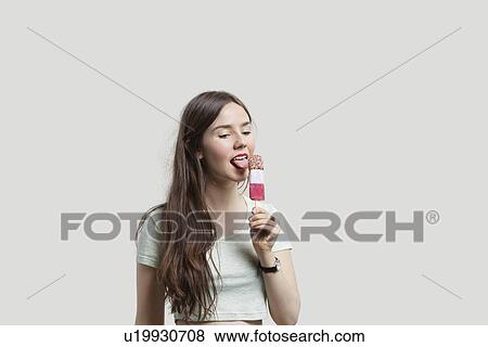 Beautiful young woman licking popsicle over gray background View Large Photo Image Stock Photo - Beautiful young woman licking popsicle over gray background. Fotosearch
