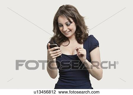 Stock Image - Beautiful young woman reading text message on cell phone over gray background. Fotosearch