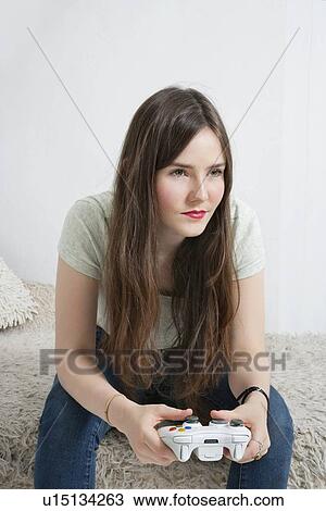 Stock Image - Beautiful young woman sitting on fur sofa with game controller. Fotosearch