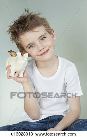 Stock Image - Boy holding a piggy bank over gray background. Fotosearch