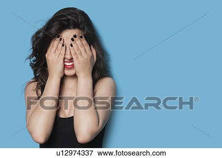Cheerful young woman covering her face against blue background View Large Photo Image Stock Photo - Cheerful young woman covering her face against blue background. Fotosearch