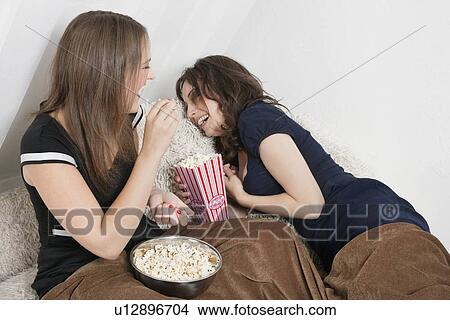 Picture - Cheerful young women eating popcorn in bed. Fotosearch