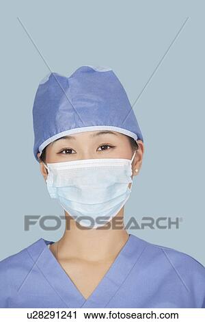 Stock Image - Close-up of a female surgeon wearing facemask over light blue background. Fotosearch