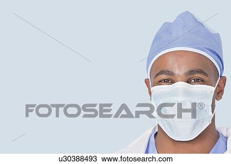 Close-up of a male doctor wearing facemask over light blue background View Large Photo Image Stock Image - Close-up of a male doctor wearing facemask over light blue background. Fotosearch