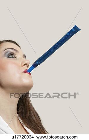 Close-up of a young woman blowing blue party blower against gray background View Large Photo Image Picture - Close-up of a young woman blowing blue party blower against gray background. Fotosearch