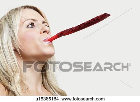 Close-up of a young woman blowing party blower against gray background View Large Photo Image Picture - Close-up of a young woman blowing party blower against gray background. Fotosearch