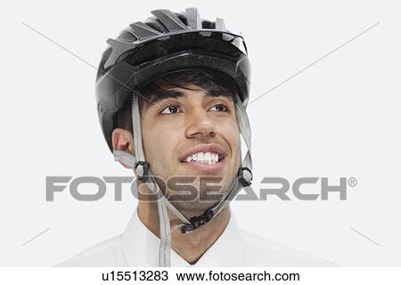 Stock Image - Close-up of Indian businessman wearing cycling helmet while looking away against gray background. Fotosearch