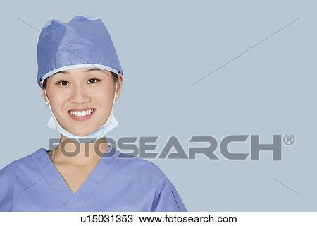 Stock Image - Close-up portrait of female surgeon smiling over light blue background. Fotosearch
