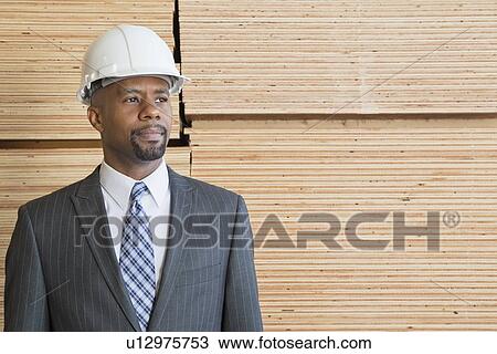 Confident African American male contractor looking away while standing in front of stacked wooden planks View Large Photo Image Stock Image - Confident African American male contractor looking away while standing in front of stacked wooden planks. Fotosearch