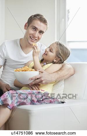 Daughter feeding wheel shape snack pellets to her father View Large Photo Image Stock Photograph - Daughter feeding wheel shape snack pellets to her father. Fotosearch
