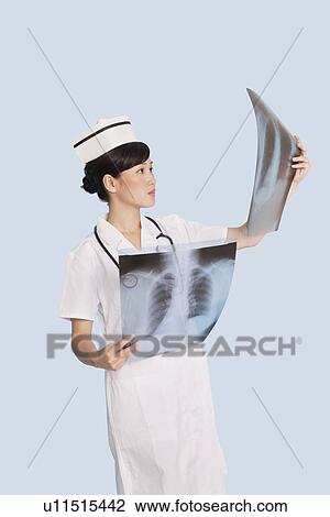 Stock Image - Female doctor analyzing x-ray reports over light blue background. Fotosearch