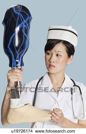 Picture - Female doctor looking at prosthesis foot over light blue background. Fotosearch