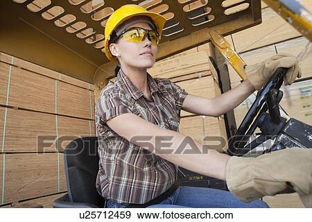 Female industrial worker driving forklift truck with stacked wooden planks in background View Large Photo Image Stock Photo - Female industrial worker driving forklift truck with stacked wooden planks in background. Fotosearch