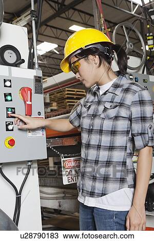 Stock Image - Female industrial worker operating manufacturing machine at factory. Fotosearch