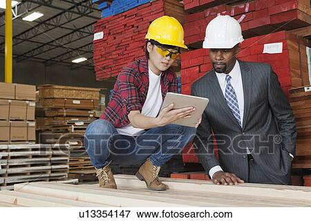 Stock Photo - Female industrial worker showing something on tablet PC to male engineer. Fotosearch