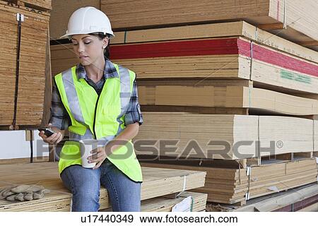 Stock Photo - Female industrial worker taking break from work at timber yard. Fotosearch