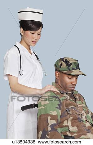 Stock Photo - Female nurse comforting disabled US Marine Corps soldier in wheelchair over light blue background. Fotosearch