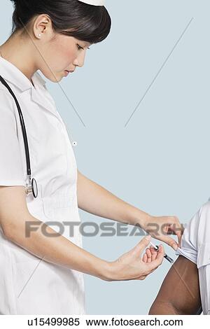Female nurse injecting patient's arm over light blue background View Large Photo Image Stock Photography - Female nurse injecting patient's arm over light blue background. Fotosearch
