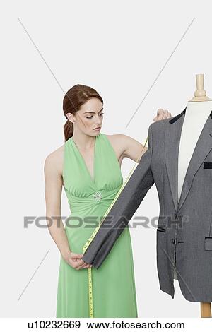 Stock Photo - Female tailor measuring sleeve of suit over gray background. Fotosearch