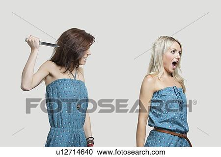 Stock Image - Friend stabbing young woman in similar jump suits from behind. Fotosearch