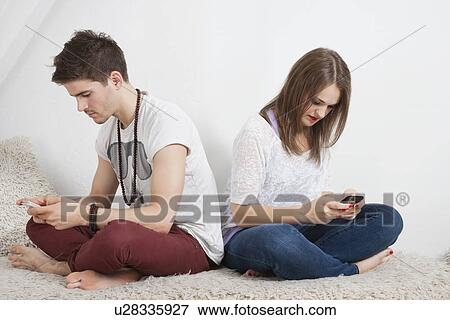 Friends text messaging with cell phone while sitting on sofa View Large Photo Image Stock Photo - Friends text messaging with cell phone while sitting on sofa. Fotosearch