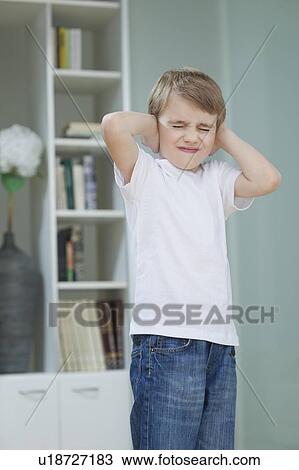 Stock Image - Frustrated boy covering his ears with hands at home. Fotosearch