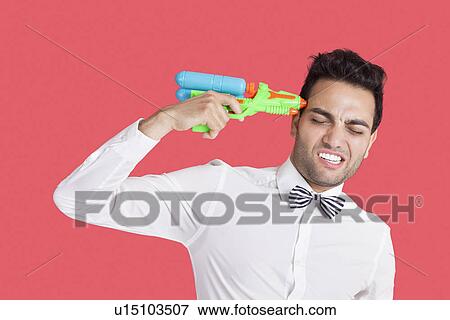 Frustrated man holding toy gun to his head over red background View Large Photo Image Stock Photo - Frustrated man holding toy gun to his head over red background. Fotosearch