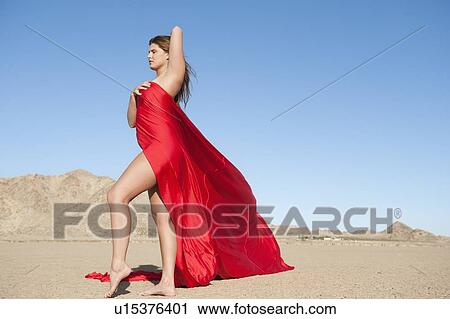Stock Image - Full length of a young woman wrapped in red cloth on arid landscape. Fotosearch