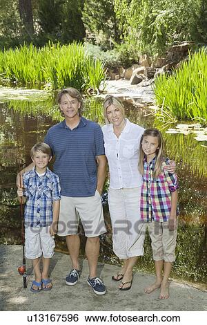 Stock Photograph - Full length portrait of couple with children standing against lake. Fotosearch
