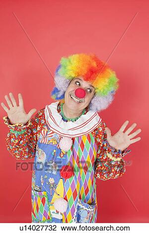 Stock Image - Funny clown with arms raised looking away against colored background. Fotosearch