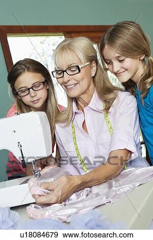 Stock Photo - Girls looking grandmother sewing cloth. Fotosearch