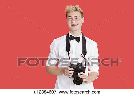 Stock Photo - Handsome young man with digital camera over red background. Fotosearch