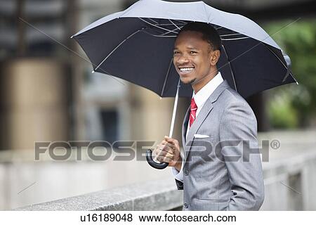 Stock Photo - Happy African American businessman holding umbrella. Fotosearch