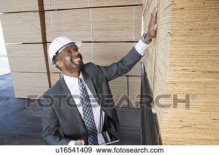Stock Photo - Happy African American male contractor inspecting wooden planks while holding tablet PC. Fotosearch