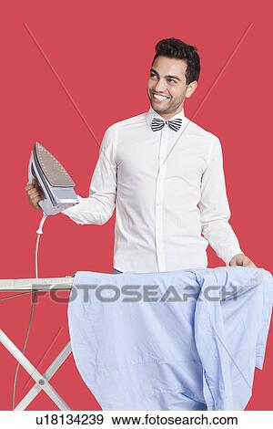 Stock Photo - Happy man in formals ironing shirt over red background. Fotosearch