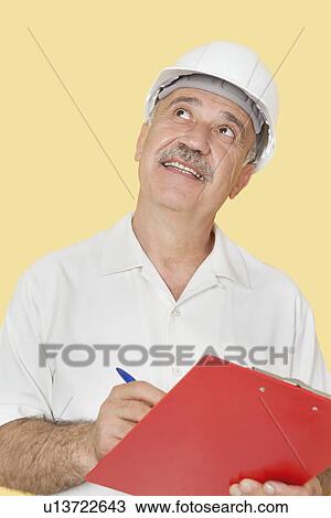 Happy senior constructor holding clipboard while looking up over yellow background View Large Photo Image Stock Image - Happy senior constructor holding clipboard while looking up over yellow background. Fotosearch
