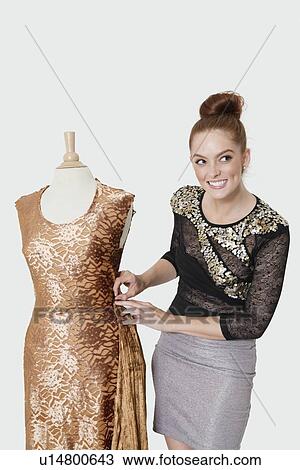 Stock Image - Happy young female fashion designer working on an outfit over gray background. Fotosearch