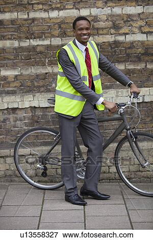 Stock Photo - Happy young male engineer with bicycle against brick wall. Fotosearch