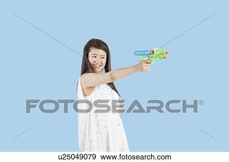 Happy young woman aiming with a toy gun over blue background View Large Photo Image Stock Photo - Happy young woman aiming with a toy gun over blue background. Fotosearch