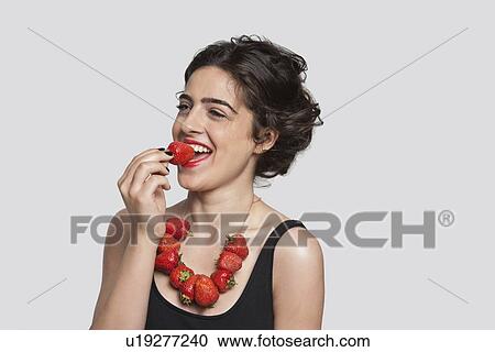 Happy young woman wearing strawberry necklace as she eats one piece over gray background View Large Photo Image Stock Image - Happy young woman wearing strawberry necklace as she eats one piece over gray background. Fotosearch