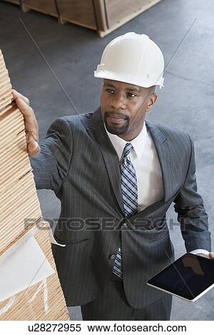 Stock Photography - High angle view of African American male contractor inspecting wooden planks while holding tablet PC. Fotosearch